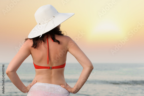 The woman on sea coast in a hat. Sunset illumination.
