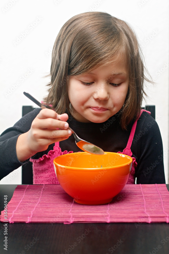 Young girl indoors eating soup from orange bowl