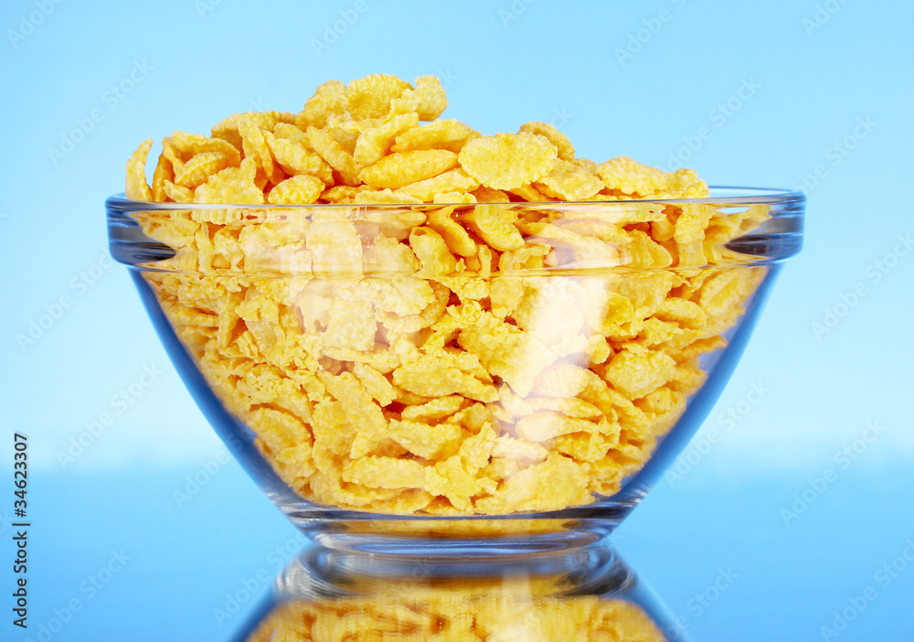 tasty cornflakes in glass bowl on blue background