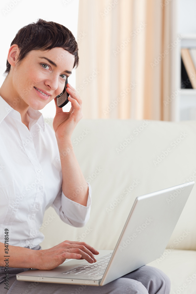 Short-haired woman with a laptop and a phone looking into the ca Short-haired woman with a laptop and a phone looking into the ca