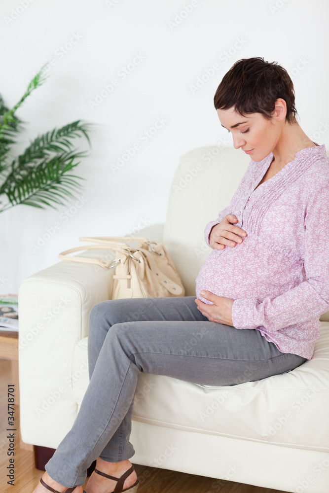 Brunette short-haired pregnant woman sitting on a sofa touching Brunette short-haired pregnant woman sitting on a sofa touching
