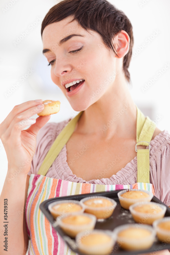 Smiling brunette woman showing muffins while eating one Smiling brunette woman showing muffins while eating one
