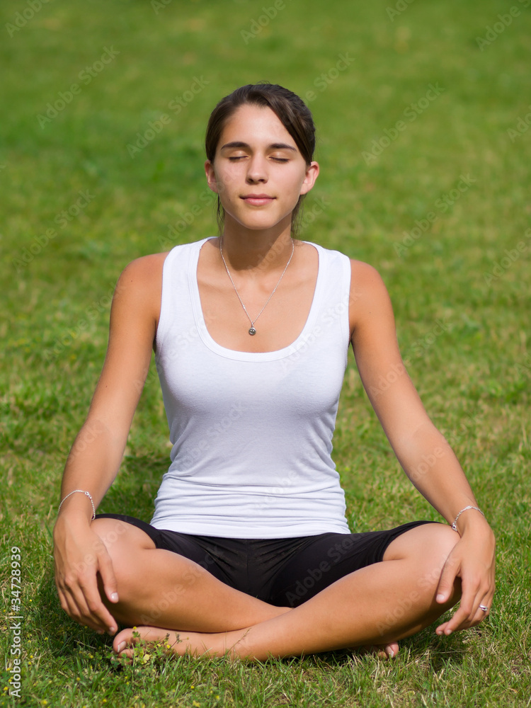 Pretty young woman meditating on grass