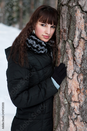 Junge sympatische Frau in Winteroutfit lehnt sich an einen Baum
