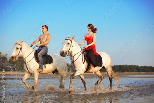 Young couple in the sea on horseback