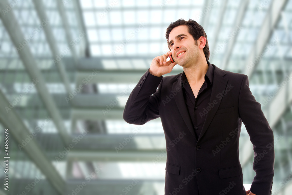 Happy young business man speaking on cellphone at a modern offic Happy young business man speaking on cellphone at a modern offic
