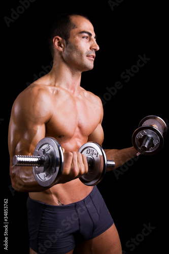 Muscular young man lifting dumbbells on black background.