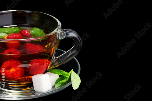 black tea, raspberry, lime and mint in cup on black background
