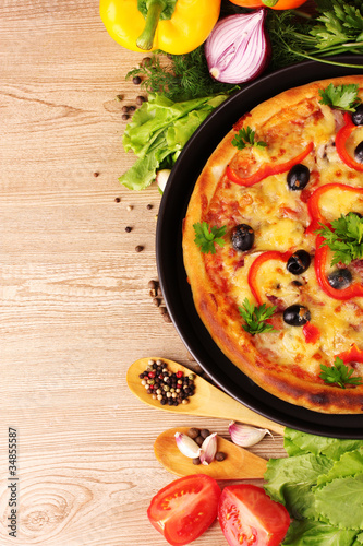 tasty pizza on the plate and vegetables on a wooden background