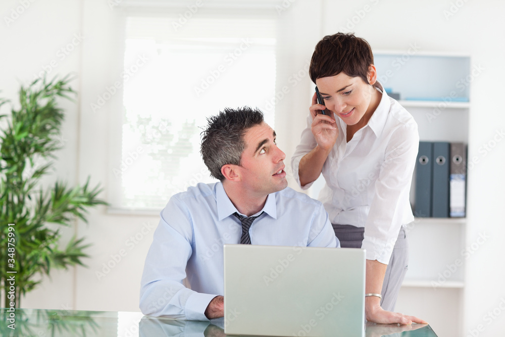 Businesswoman making a phone call while her colleague is working