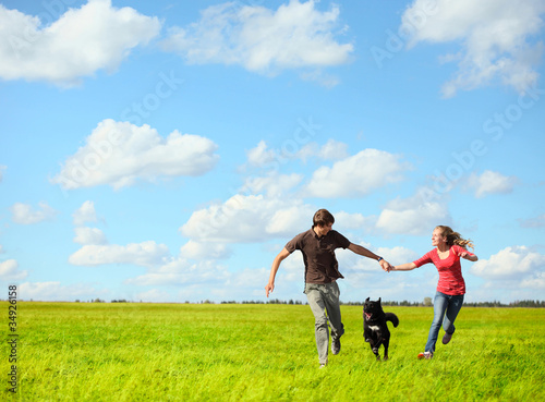 Young happy family running with dog on a green meadow