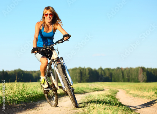 Young woman riding on a bicycle on a countryside road © Dudarev Mikhail