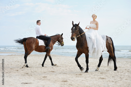 Beach wedding: bride and groom on a horses by the sea