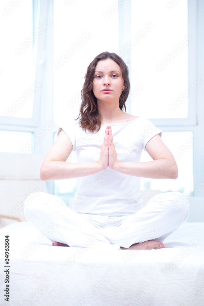 Young woman meditating with closed eyes in bright bedroom sittin