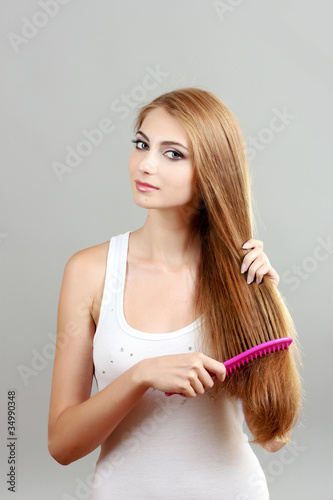 Beautiful young girl with hairbrush on gray background