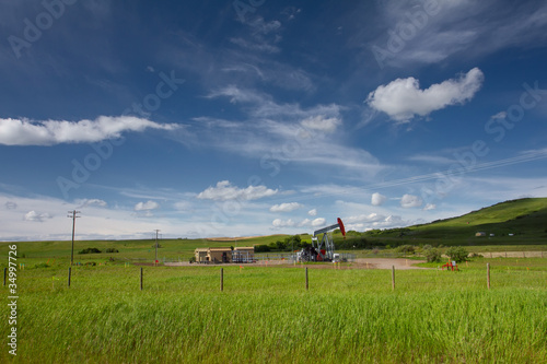 Canadian landscape with green grass, blue sky and pumpjack