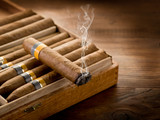 smoking cuban cigar over box on wood background