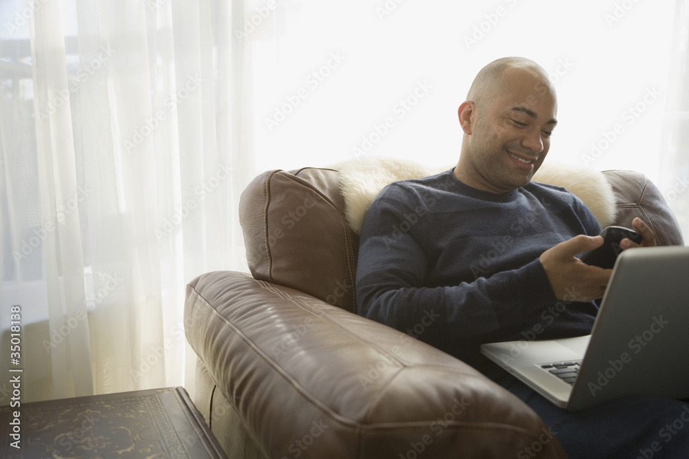 Mixed race man with laptop using cell phone Mixed race man with laptop using cell phone
