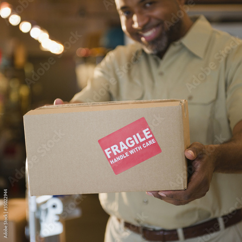 African American deliveryman holding out box with “fragile” sticker