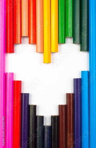 Colored pencils in heart shape on white