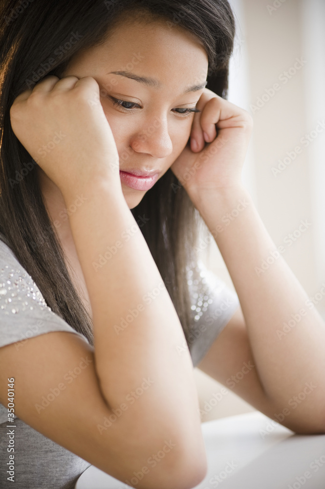 Sad mixed race teenage girl looking down with head in hands Sad mixed race teenage girl looking down with head in hands
