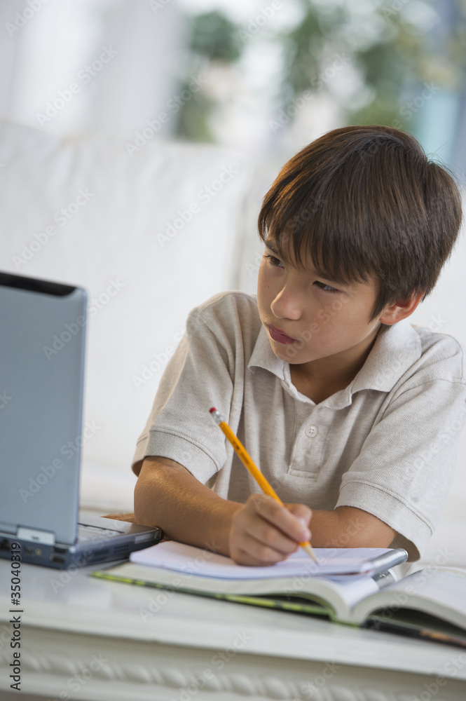 Mixed race boy doing homework and looking at laptop Mixed race boy doing homework and looking at laptop