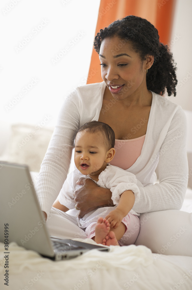 Mixed race woman holding baby and using laptop Mixed race woman holding baby and using laptop