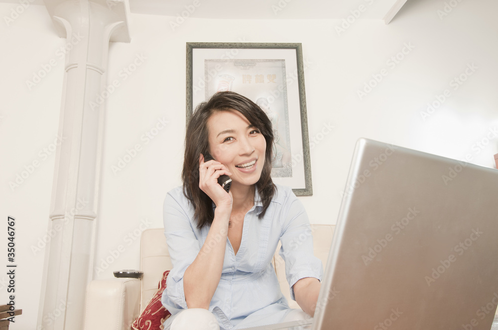 Korean woman using laptop and talking on phone in living room Korean woman using laptop and talking on phone in living room
