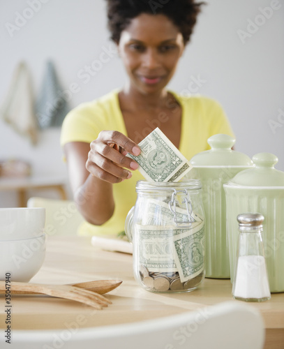 Black woman putting money in jar photo