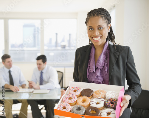 African American businesswoman carrying box of donuts photo