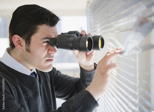 Hispanic businessman peering through window with binoculars photo