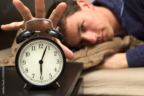 Alarm clock with male model in bed in background.