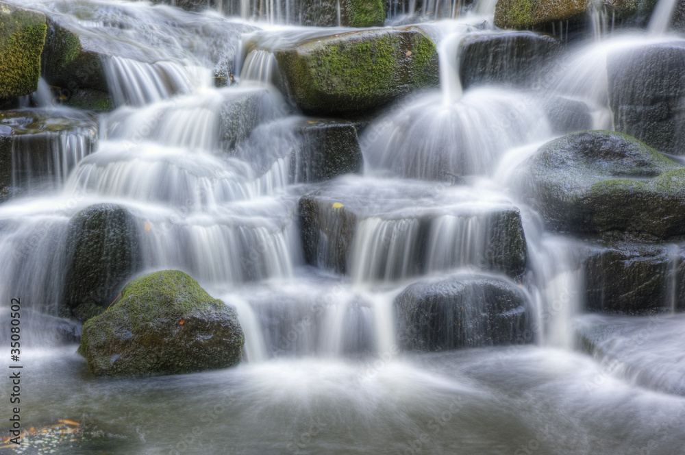Fototapeta premium Beautiful waterfall cascades over rocks in lush forest landscape