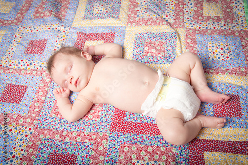 Sleeping baby boy in diaper on colorful quilt