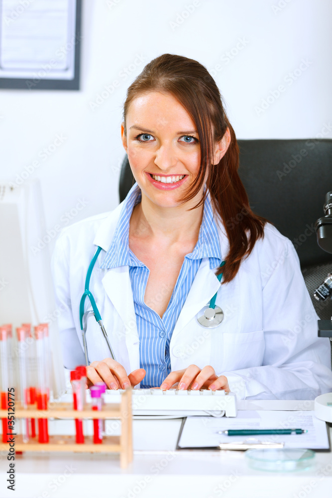 Smiling doctor woman sitting at table and working on computer Smiling doctor woman sitting at table and working on computer