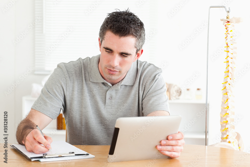 Man sitting at a table with a tablet and a chart Man sitting at a table with a tablet and a chart