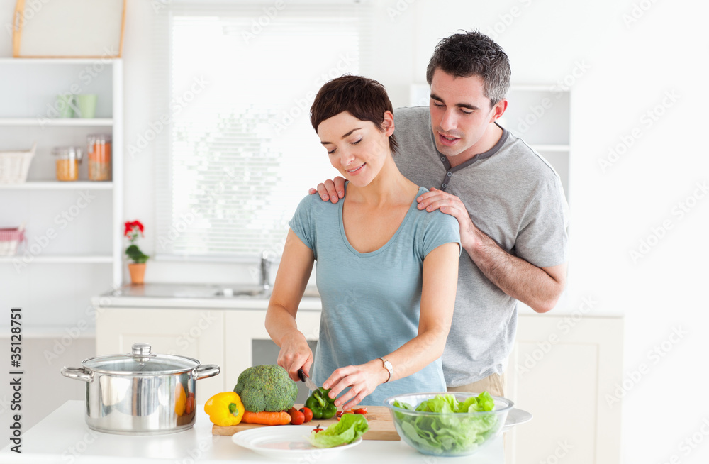 Man massaging his wife while she is cutting vegetables Man massaging his wife while she is cutting vegetables
