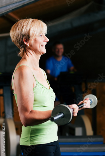 Ältere Frau macht Sport mit Langhantel im Fitnessstudio