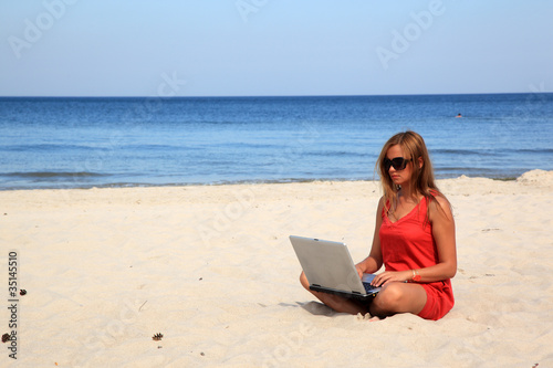 Young woman with laptop is sitting on the sunny beach.
