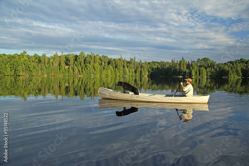 Billede på lærred Canoeist with Dog in the Bow and Beautiful Reflection