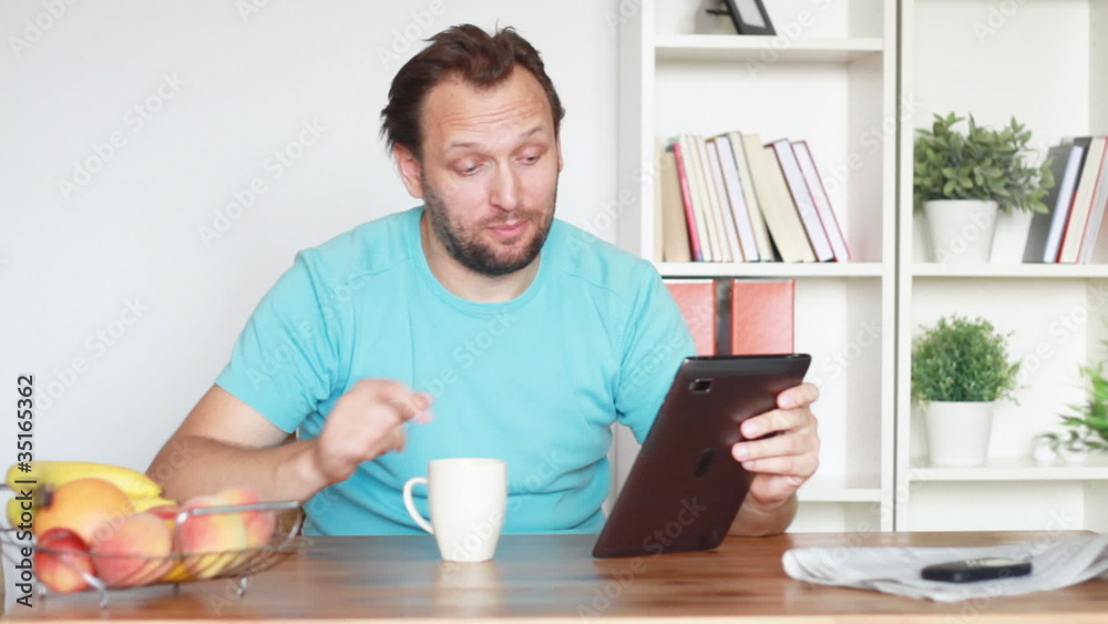 Young man chatting on tablet computer by the table in home Young man chatting on tablet computer by the table in home