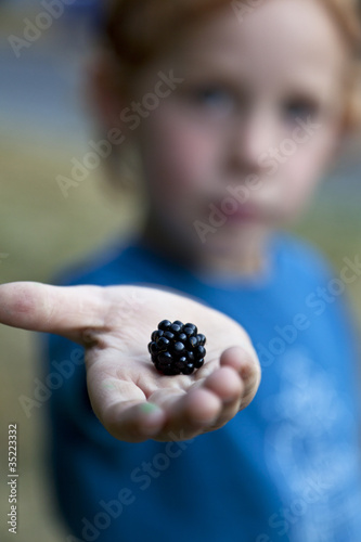 A young boy holding out a blackberry