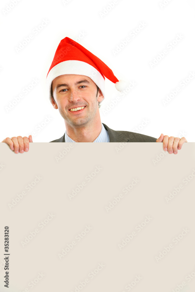 Smiling guy in Santa hat holding blank billboard Smiling guy in Santa hat holding blank billboard