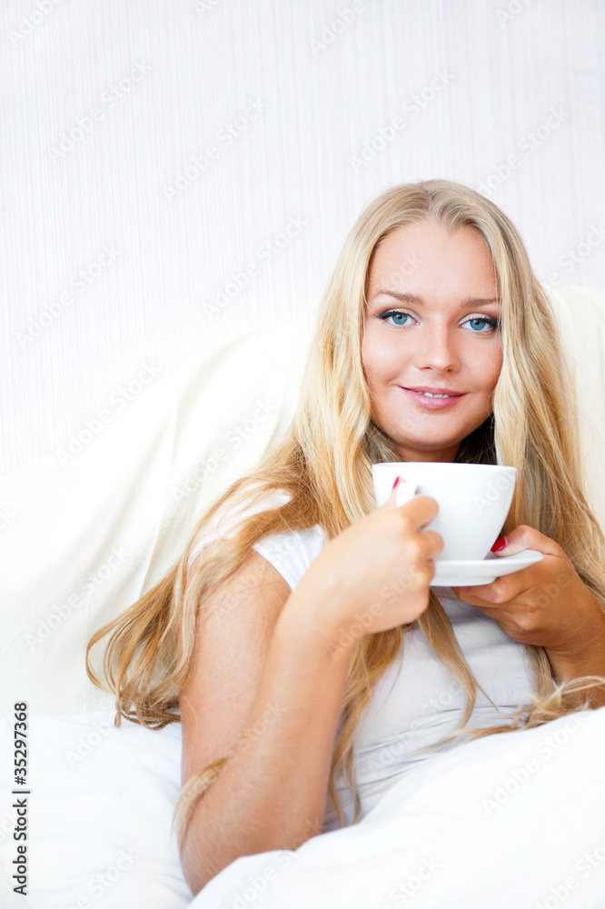 Smiling woman drinking a coffee lying on a bed at home or hotel. Smiling woman drinking a coffee lying on a bed at home or hotel.