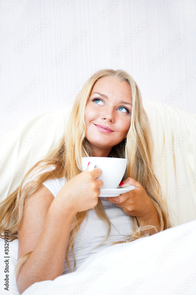 Smiling woman drinking a coffee lying on a bed at home or hotel. Smiling woman drinking a coffee lying on a bed at home or hotel.