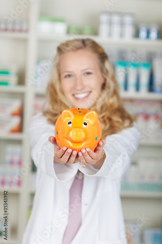 lächelnde apothekerin zeigt sparschwein photo