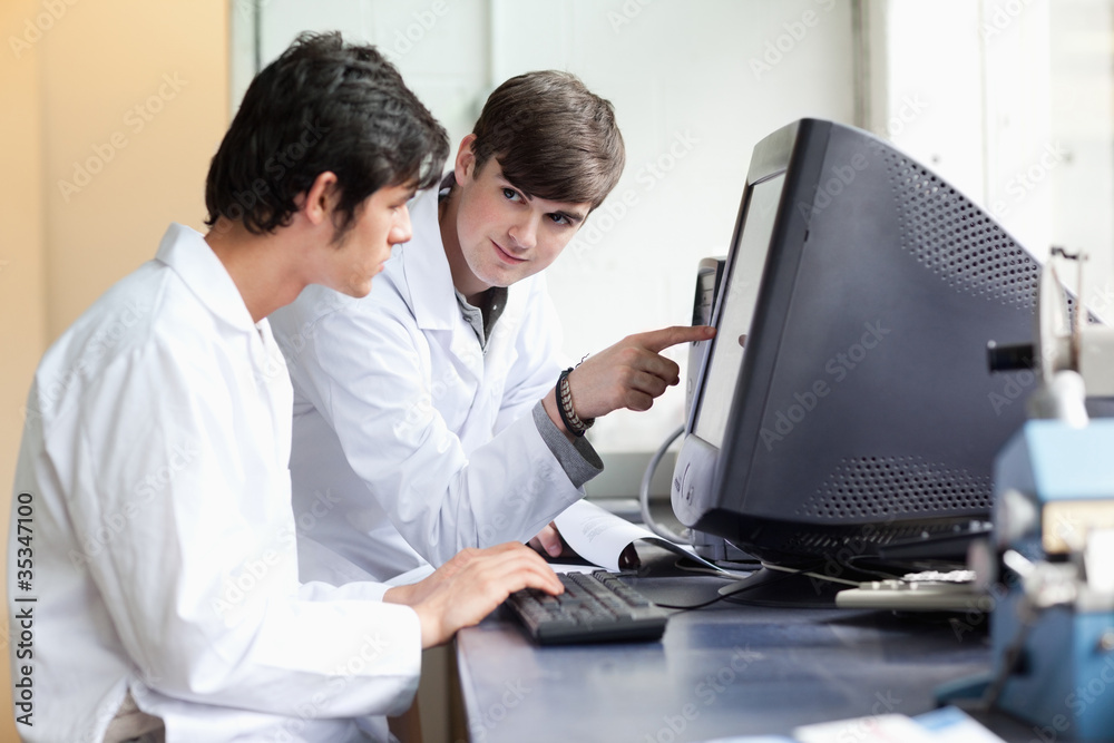 Student pointing at something on a monitor to his classmate Student pointing at something on a monitor to his classmate