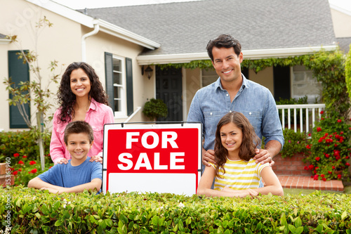 Hispanic family outside home with for sale sign