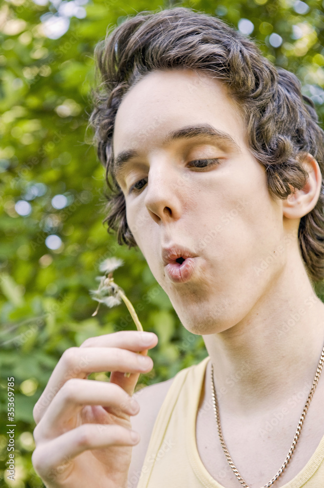 Young man blowing on a dandelion Young man blowing on a dandelion