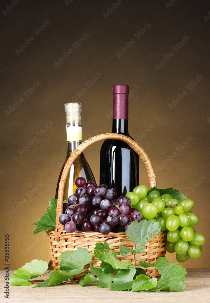 Bottles of wine and grapes in basket on yellow background